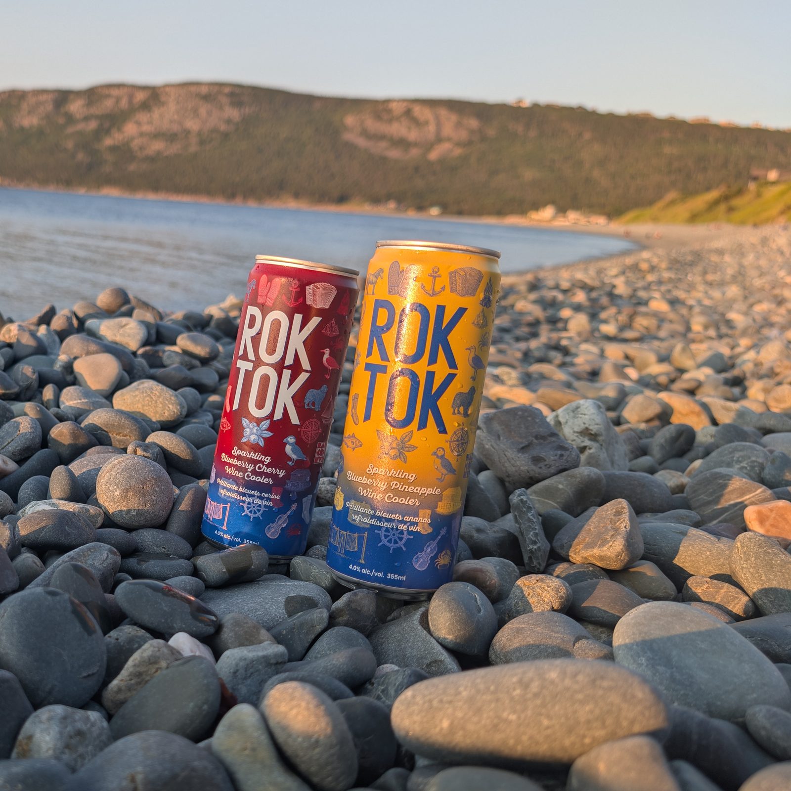 Two ROK TOK sparkling wine cooler cans standing on beach rocks by the water in Newfoundland